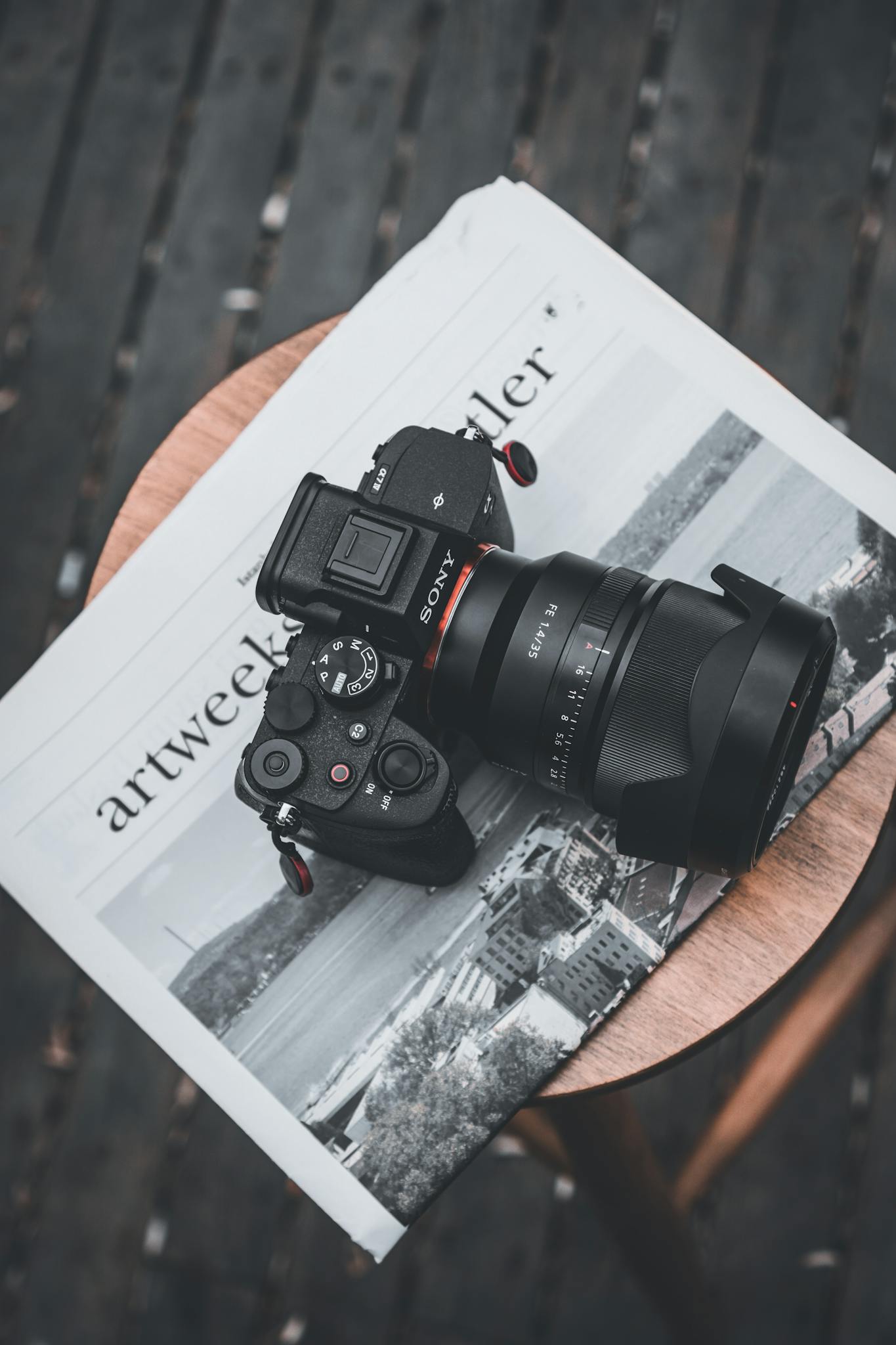 Top view of a DSLR camera resting on a newspaper placed on a wooden stool.
